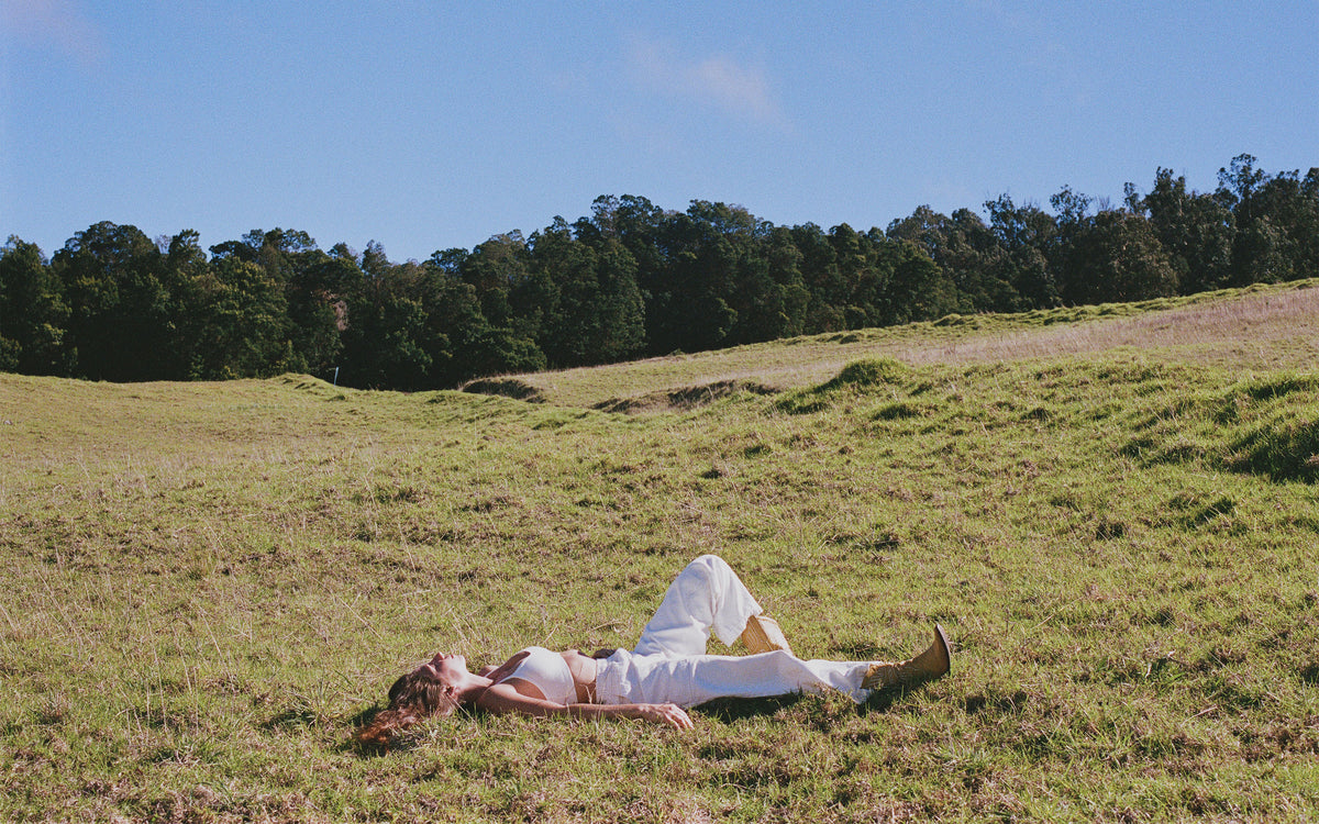 A woman in a white outfit lies on her back on a grassy hill